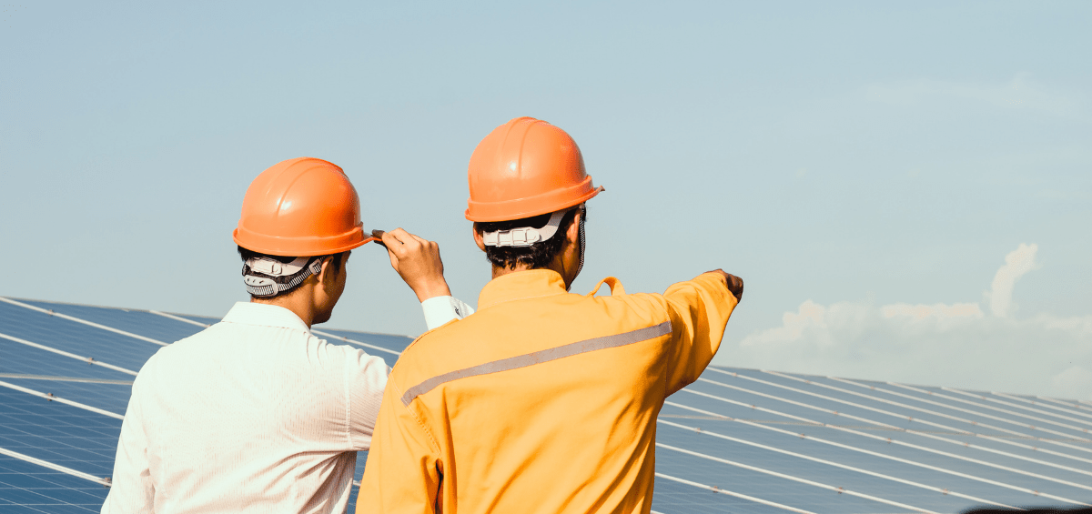 Two men in hard hats next to a solar panel