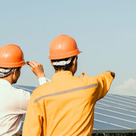 Two men in hard hats next to a solar panel